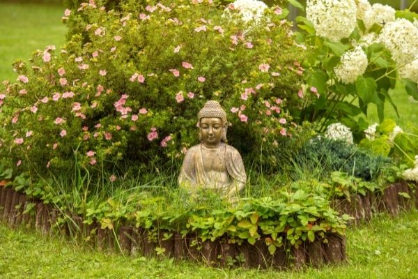 small Buddha in garden framed by flowering shrub